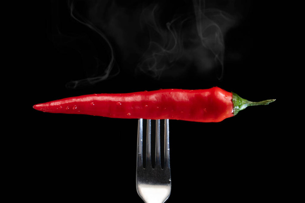 hot red pepper with steam on a fork on a black background - Photo, Image