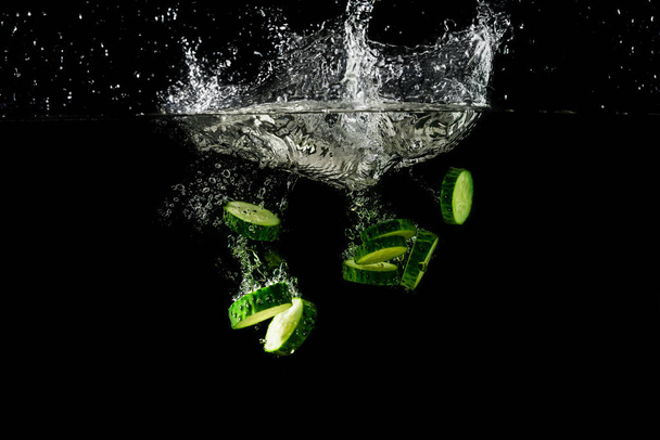 de plakjes komkommer vallen in water. - Foto, afbeelding