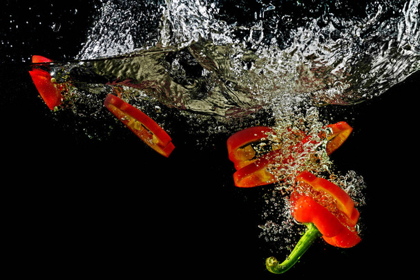 Red fresh paprika slices splash in water on a black background. - Zdjęcie, obraz