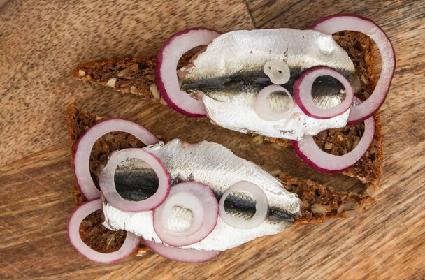 Sprat on a piece of black bread. Fish with bread and red onion on a cutting table. - Photo, Image