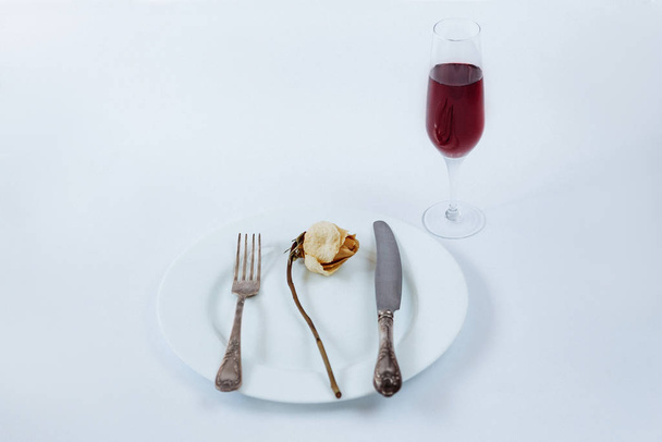 White plate with dried rose, fork, knife and glass of champagne on a white background - Photo, Image