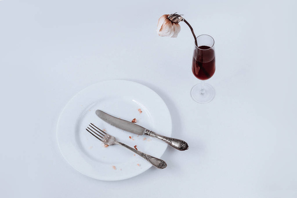 White plate with fork, knife and glass of champagne with the dried rose on a white background - Photo, Image