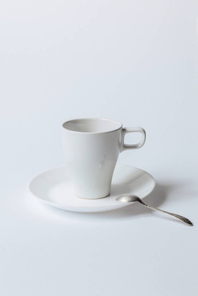 weiße Kaffeetasse auf einer Untertasse und der metallische Teelöffel isoliert auf weißem Hintergrund - Foto, Bild