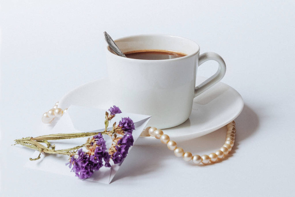 ein Stillleben mit einer weißen Keramiktasse Kaffee, einer Korallenkette und den getrockneten Blumen - Foto, Bild