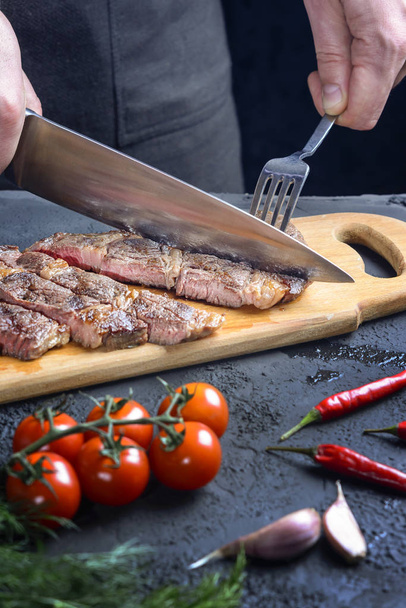 The process of cutting a steak into pieces. Chef with fork and knife. Cropped photo - Foto, afbeelding