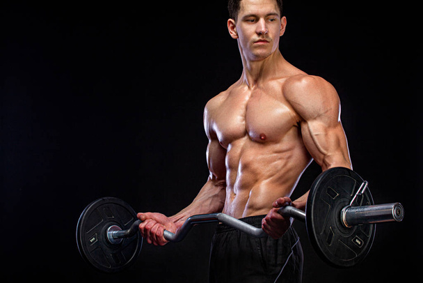 Athlete bodybuilder. Brutal strong muscular athletic man pumping up muscles with barbell on black background. Workout bodybuilding concept. - Foto, Imagem