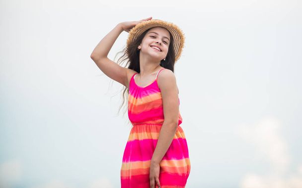 Happy vacation. Happy childhood. Enjoying relax. Child happy small girl. Free and carefree. Good vibes. Happy international childrens day. Cute girl in summer dress and hat outdoors sky background - Fotó, kép