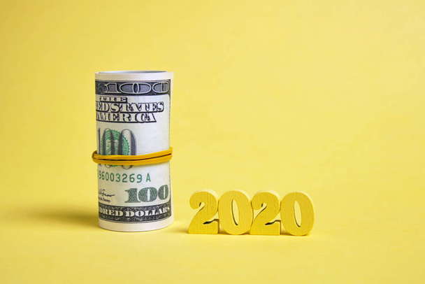 Figuras de madeira 2020 em um fundo amarelo com um rolo de dólares amarrado com uma faixa elástica
. - Foto, Imagem