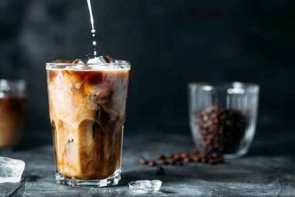 Milk Being Poured Into Iced Coffee on a dark table - Фото, изображение