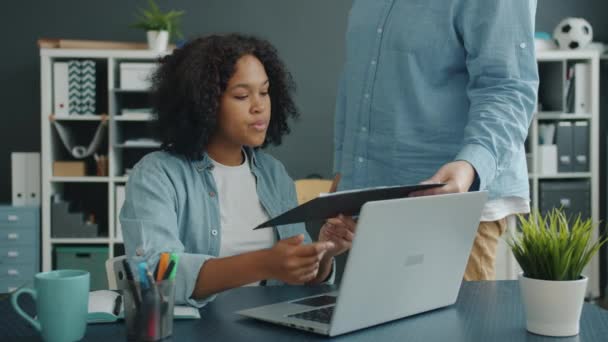 Attractive Afro-American lady taking documents from male colleague then using laptop - Footage, Video