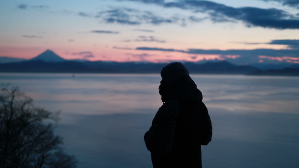 Man Takes a Picture with His Smartphone in a Snowy Wild Landscape at Sunset (em inglês). Backview de um indivíduo adulto solitário que passa o tempo pelo ir e olhar ao redor nas fotos de beleza da área de praia selvagem
. - Filmagem, Vídeo
