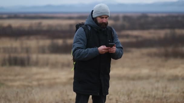 Man with beard, wearing winter clothes talking on the phone. A hiker goes in the winter mountains with a backpack. Beautiful mountains in winter time - Video, Çekim