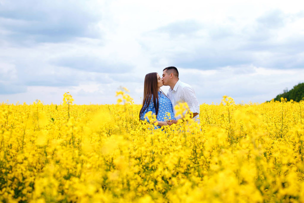 A pregnant girl and her boyfriend stand in a field of rapeseed and enjoy the spring weather, future parents spend time outdoors - Foto, Imagem