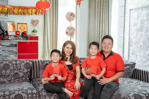 Asian chinese family with two son holding ang pao smiling when sitting on sofa - Фото, изображение