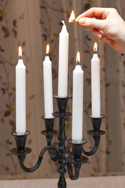 Hořící svíčky v retro svícnu stojí na stole v pokoji. žena zapaluje svíčky. Romantická atmosféra. Černý svícen. Pěkná výzdoba. Starý nebo starožitný styl. - Fotografie, Obrázek