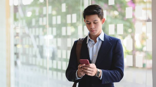 Cropped shot of businessman texting on smartphone while standing in office room - Photo, Image