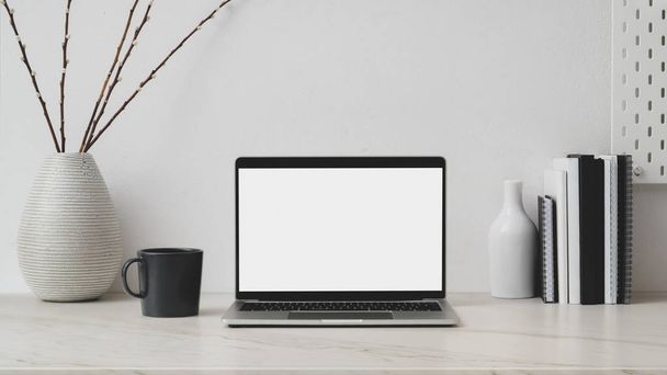 Schnappschuss vom Arbeitsplatz mit leerem Bildschirm-Laptop, Dekorationen, Büchern und Kaffee auf Marmorschreibtisch mit weißer Wand - Foto, Bild