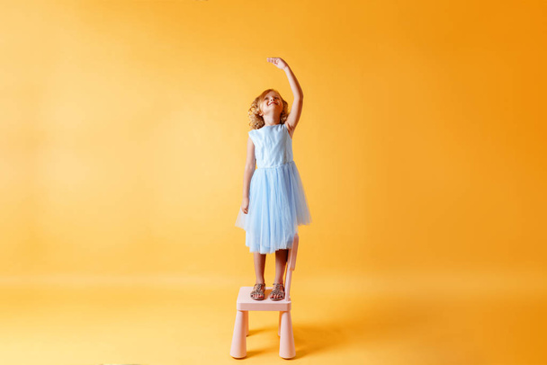 A little child girl in a blue dress is standing on a chair and m - Foto, immagini