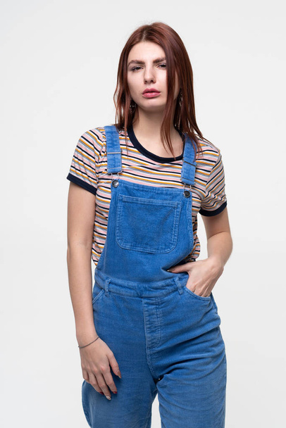young beautiful girl posing in studio, standing in blue overalls - Photo, Image