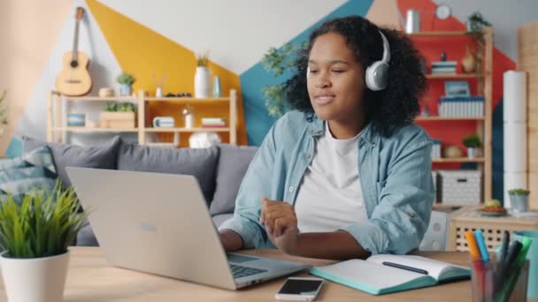 Pretty lady in headphones listening to music in apartment enjoying song typing on laptop - Footage, Video