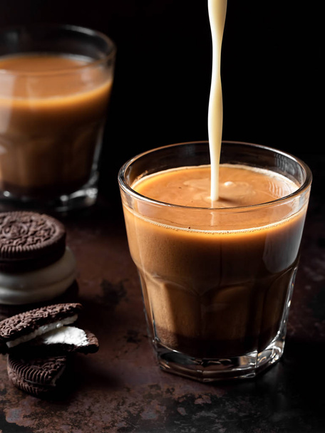 Deux verres de café au lait, à côté des biscuits au chocolat. Le lait est versé dans un verre avec une boisson. Le café est situé sur un fond métallique foncé. Gros plan, orientation verticale. Profondeur superficielle de fie
 - Photo, image