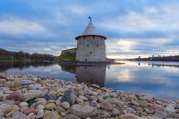 The watchtower of the Pskov Kremlin reflected in water.  In the foreground are stones of different sizes. - Foto, immagini