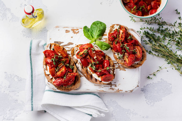 Sandwiches with baked cherry tomatoes and cottage cheese, thyme, garlic and herbs on an old light vintage background. Top view.  - Foto, Imagem