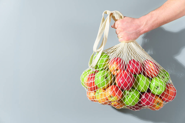 Mies käsi pitää merkkijono laukku punainen ja vihreä omenat
. - Valokuva, kuva