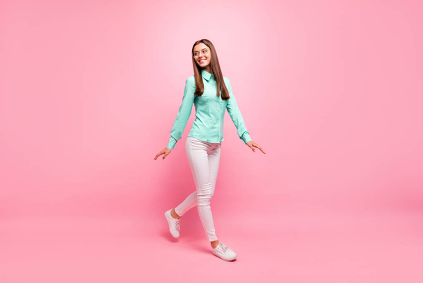 Full body photo of funny pretty lady walking down street enjoy sunny day weather wear specs turquoise shirt white trousers isolated pink color background - Фото, изображение