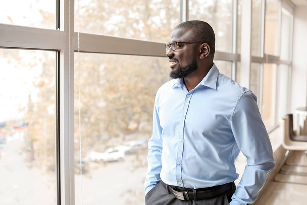 Πορτρέτο του όμορφου Αφροαμερικανού επιχειρηματία κοντά στο παράθυρο στο γραφείο - Φωτογραφία, εικόνα