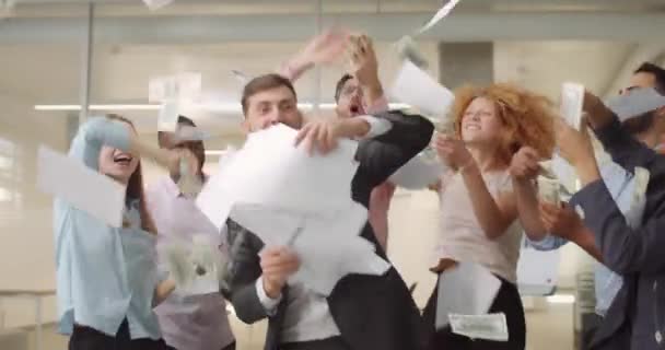 Male and female office team celebrating successful meeting. Happy employees throwing up documents and banknotes while dancing in working space. Concept of success and good mood. - Video, Çekim