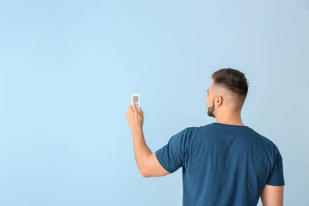 Young man with air conditioner remote control on color background - Photo, image
