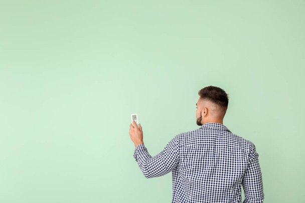 Jonge man met de afstandsbediening van de airconditioner op kleur achtergrond - Foto, afbeelding