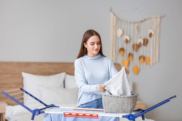 Beautiful young woman hanging laundry on clothes dryer - Фото, изображение
