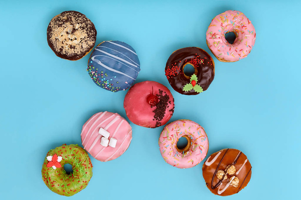 Sweet colored donuts on a blue background, laid out in the form of various geomitric figure, arrow, square, line, triangle, top view. Desserts, game of colors, blue background. - Фото, изображение