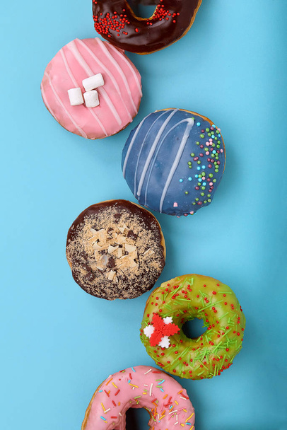 Sweet colored donuts on a blue background, laid out in the form of various geomitric figure, arrow, square, line, triangle, top view. Desserts, game of colors, blue background. - Photo, Image