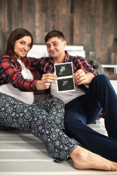 Happy and excited pregnant couple looking at the ultrasound images of their baby lying on the bed - Фото, зображення