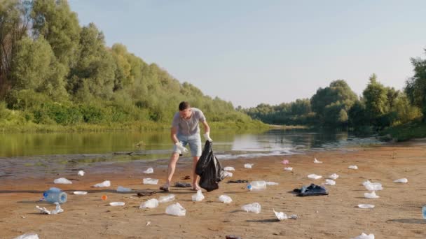 Man collects plastic trash on the banks of polluted river and listens to music - Imágenes, Vídeo