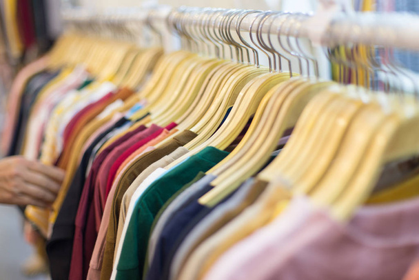 рука людей выбирают красочные футболки на вешалке для одежды
 - Фото, изображение