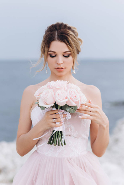 Retrato de una joven novia hermosa con un ramo de rosas cerca del mar
. - Foto, Imagen