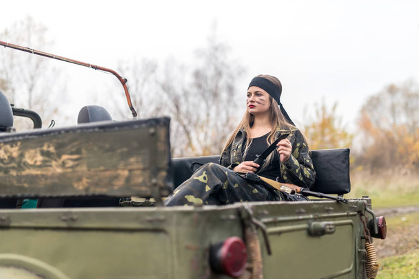 Mujer soldado con rifle posando cerca de coche militar
 - Foto, Imagen