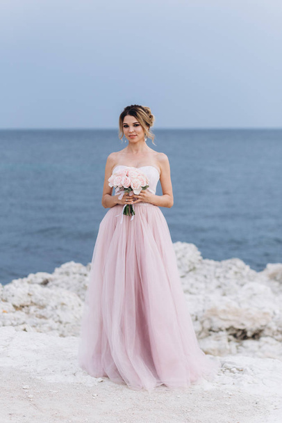 Porträt einer jungen schönen Braut mit einem Strauß Rosen am Meer. - Foto, Bild