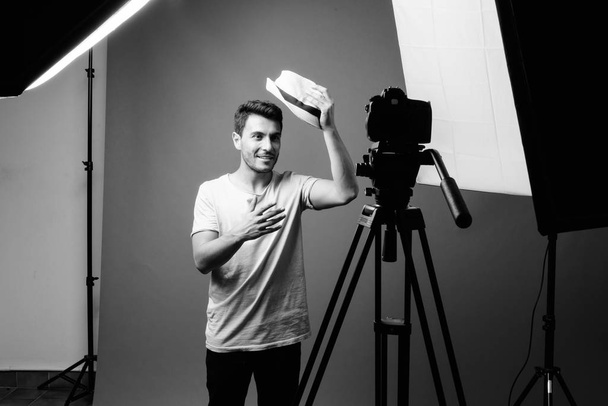 Estudio de un joven guapo hombre hispano vlogging con cámara sobre fondo gris en blanco y negro - Foto, Imagen