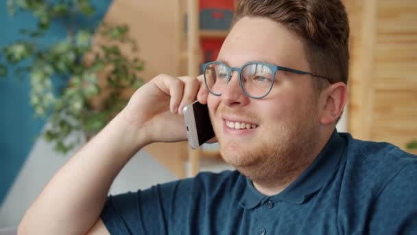 Joyful young man talking on mobile phone in apartment enjoying conversation - Felvétel, videó