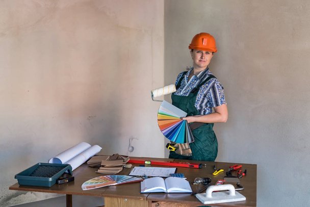 Mulher de uniforme protetor mostrando ferramentas de pintura
 - Foto, Imagem