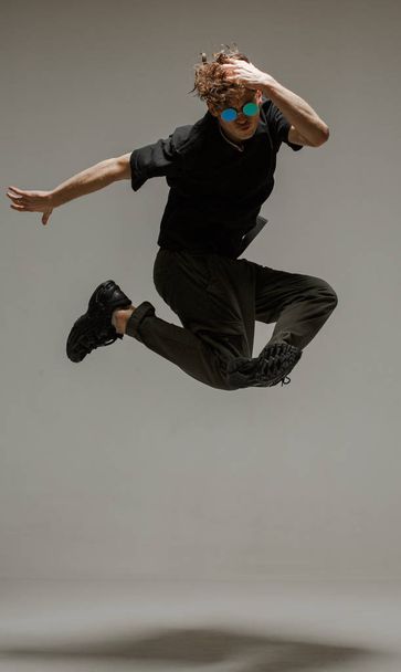 Guy dancing contemporary dance in studio. Neutral grey background. Acrobatic bboy dancer. - Foto, Imagen