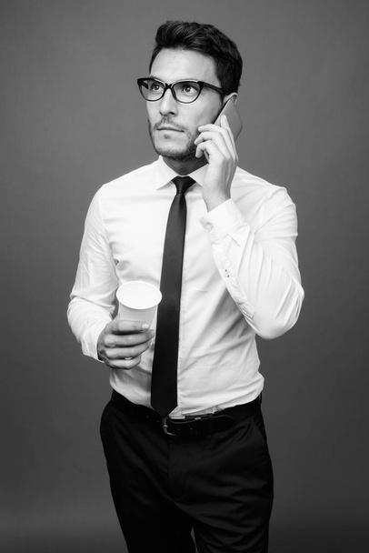 Studio shot of young handsome Hispanic businessman against gray background in black and white - Fotoğraf, Görsel