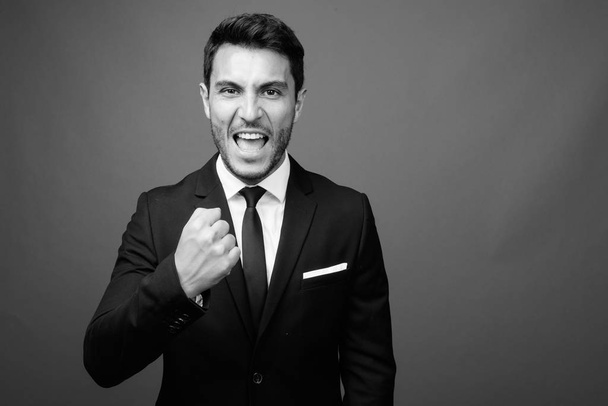 Studioaufnahme eines jungen, gut aussehenden hispanischen Geschäftsmannes im Anzug vor grauem Hintergrund in schwarz-weiß - Foto, Bild
