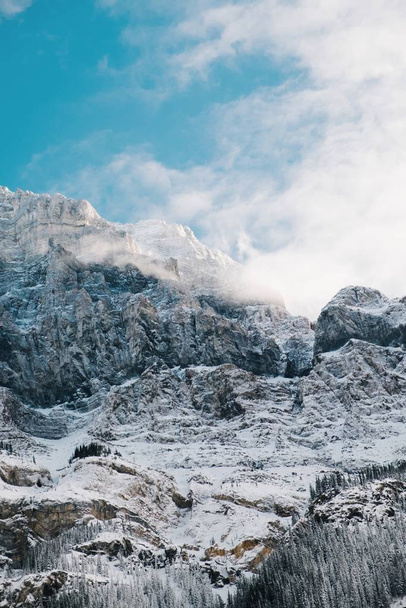 Vertical shot of the rocks covered with snow under the bright cloudy sky - Φωτογραφία, εικόνα