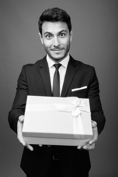 Studioaufnahme eines jungen, gut aussehenden hispanischen Geschäftsmannes im Anzug vor grauem Hintergrund in schwarz-weiß - Foto, Bild